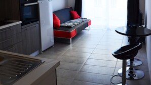 A compact kitchen with modern appliances, a dining area with a small table and two bar stools, and a sofa with red cushions. - Elegant F1 all comfort, quiet city center terrace, parking 10 min center<br> (Ajaccio)