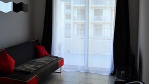 A modern living room with a sofa, a small table, and a view through a window with sheer curtains. - Elegant F1 all comfort, quiet city center terrace, parking 10 min center<br> (Ajaccio)