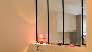A bedroom with a bed, a bedside table with a lamp, a mirror, and a wall with a sign that reads "Love begins at home." - Elegant F1 all comfort, quiet city center terrace, parking 10 min center<br> (Ajaccio)