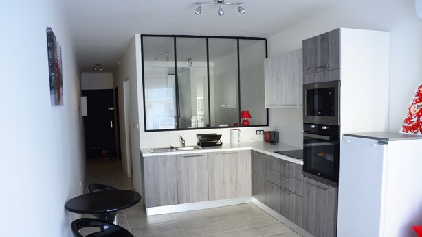 A modern kitchen with grey cabinets, a white countertop, a black refrigerator, and a black microwave. There is a small dining area with two black chairs. - Elegant F1 all comfort, quiet city center terrace, parking 10 min center<br> (Ajaccio)