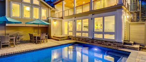 Ein zweistöckiges Haus mit Swimmingpool, Sitzgelegenheiten im Freien und einem Balkon.