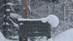 Un letrero de madera con el texto 'Welcome to Pine Creek Cove Cabin' y un número de teléfono.