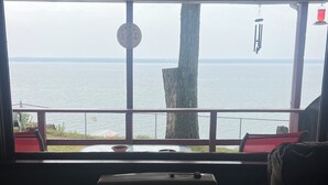 A room with a large window overlooking a body of water, a wooden ceiling, and a radiator.
