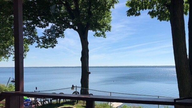 A view from a covered deck overlooking a calm lake with a clear sky.