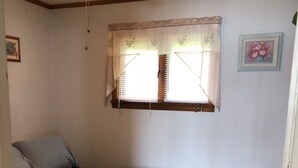 A bedroom with a single bed, a ceiling fan, a window with curtains, and a framed picture on the wall.