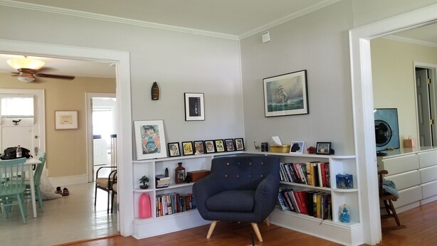A living room with a bookshelf, a blue armchair, and a dining area with a table and chairs. - Adorable Cape Cod House in a Little Fishing Town (Marshallberg)