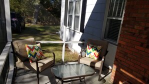 An outdoor patio with two cushioned chairs and a glass table, surrounded by a brick wall and white siding. - Adorable Cape Cod House in a Little Fishing Town (Marshallberg)
