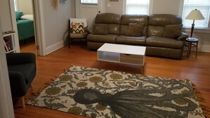 A living room with a brown leather sofa, a white coffee table, a patterned rug, and a small side table with a lamp. - Adorable Cape Cod House in a Little Fishing Town (Marshallberg)