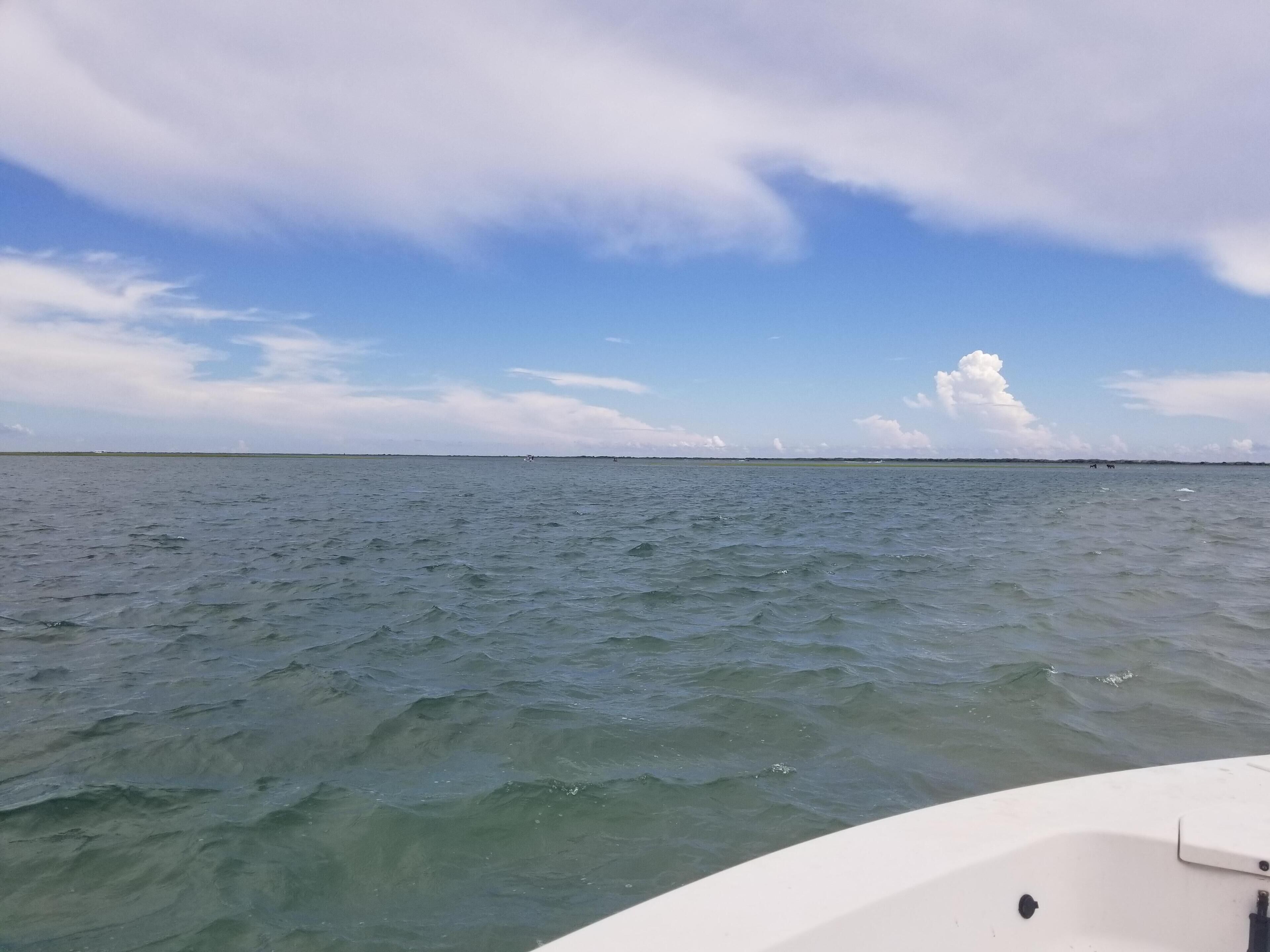 Un bateau sur une eau calme, sous un ciel dégagé, avec une terre lointaine à l’horizon.