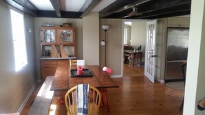 A spacious kitchen with wooden floors, a dining table with chairs, a refrigerator, and a cabinet with glass doors.