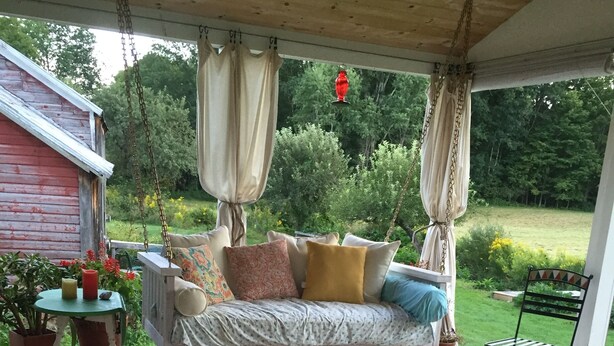 A wooden deck with a swing chair, a cushioned bench, and a small table with potted plants.