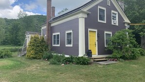 A two-story house with a yellow front door, a brick chimney, and a well-maintained lawn.