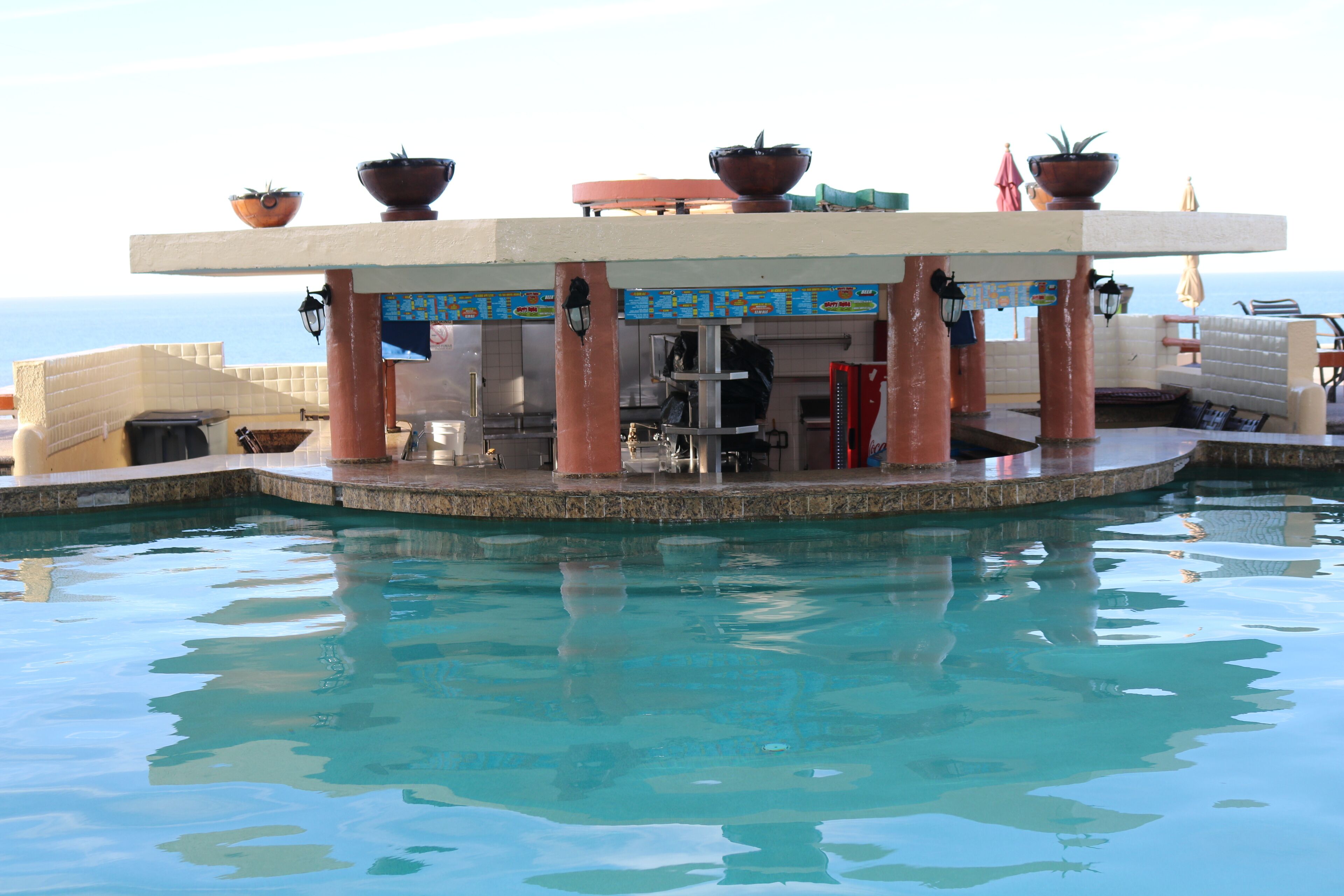 Un bar situé au bord de la piscine, avec vue sur la mer, ainsi qu’un espace détente et une piscine.