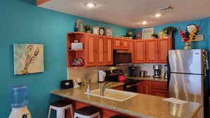 A kitchen with teal walls, wooden cabinets, a stainless steel refrigerator, and a granite countertop. - As seen on HGTV! Sonoran Sea, Beach Front, Stunning Ocean Views,2B/2B, 8th Floor (Puerto Peñasco)