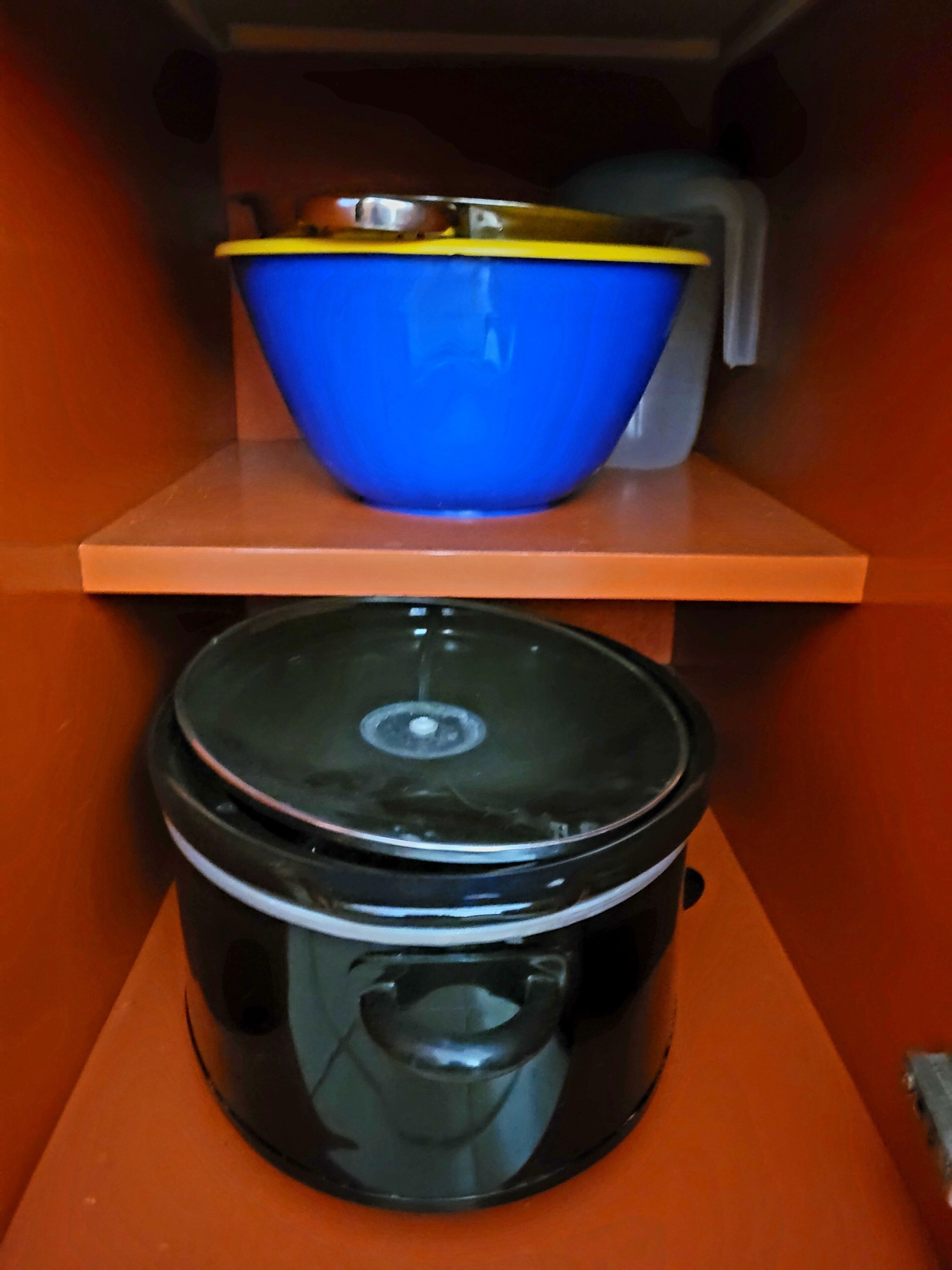 Una cocina con una olla de cocción lenta negra sobre la encimera y un tazón azul en un estante superior.