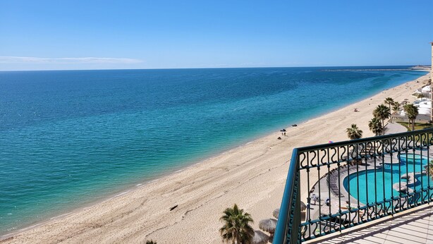 A beach view with a pool area, palm trees, and a clear blue sky. - As seen on HGTV! Sonoran Sea, Beach Front, Stunning Ocean Views,2B/2B, 8th Floor (Puerto Peñasco)