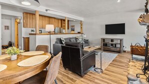 Un salon moderne avec une table à manger en bois, un canapé en cuir et un téléviseur à écran plat fixé au mur.