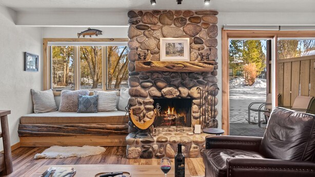 Un salon chaleureux avec une cheminée en pierre, un coin salon confortable et une vue sur l’extérieur.