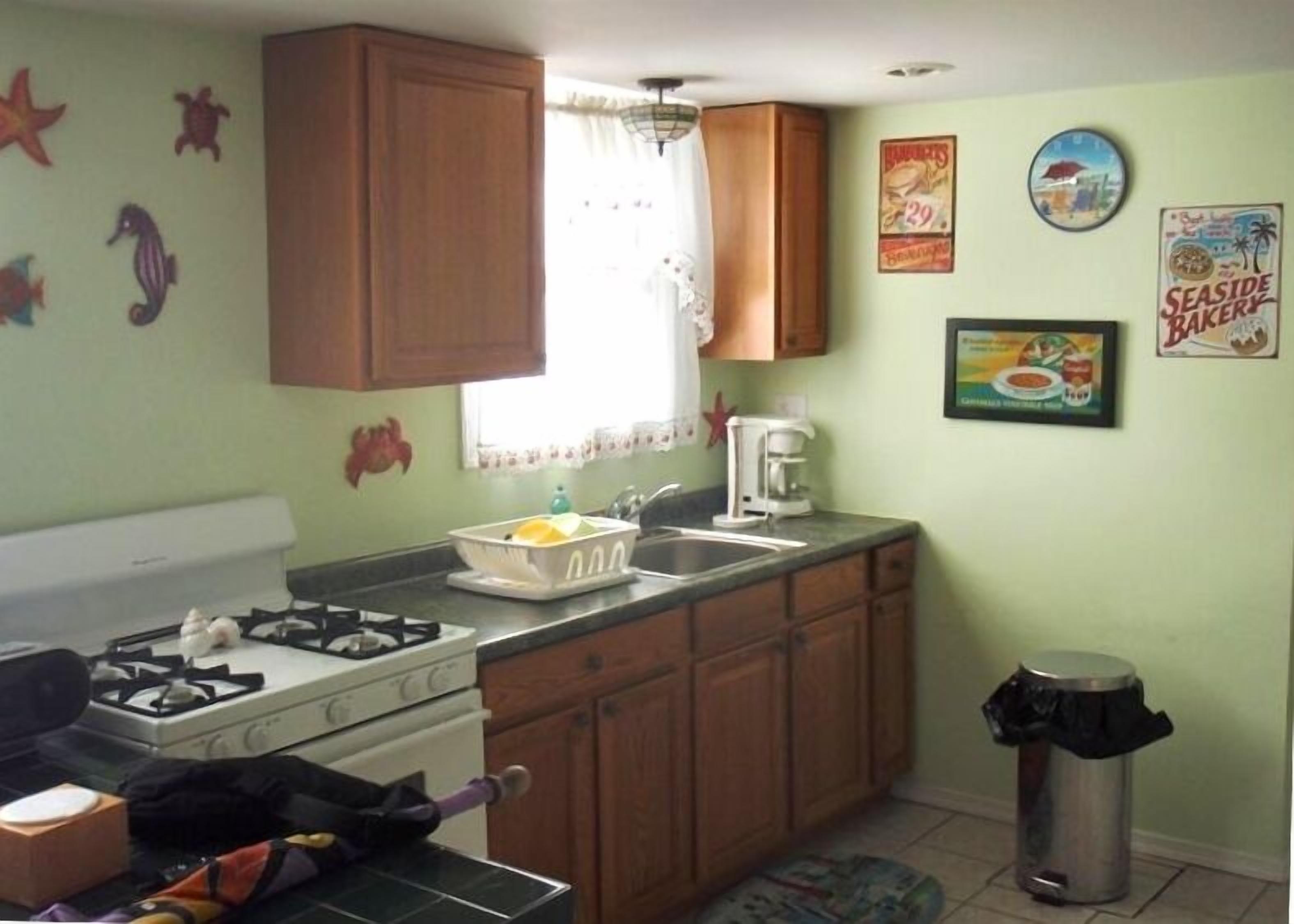 Cocina compacta con estufa a gas, pileta y alacenas de madera. Se observan adhesivos decorativos en la pared y un póster.