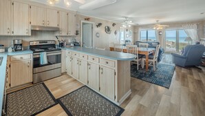 A spacious kitchen with wooden cabinets, a central island, and a dining area with a view of the ocean. - Loony Dunes | Direct Beach Access + Sound Front Dock (Topsail Beach)