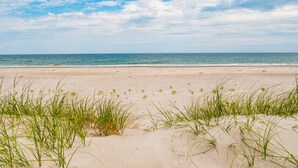 A beach with sand and grass in the foreground and a clear sky with clouds in the background. - Loony Dunes | Direct Beach Access + Sound Front Dock (Topsail Beach)
