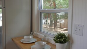 A kitchen with a wooden countertop, white cabinets, a window with a view of trees, and a refrigerator.