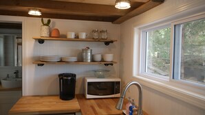 A kitchen with wooden shelves, a microwave, a sink, and a washing machine.