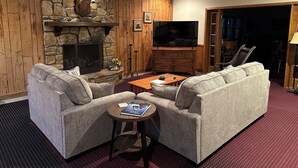 Een gezellige woonkamer met een stenen open haard, een televisie en comfortabele zitplaatsen.