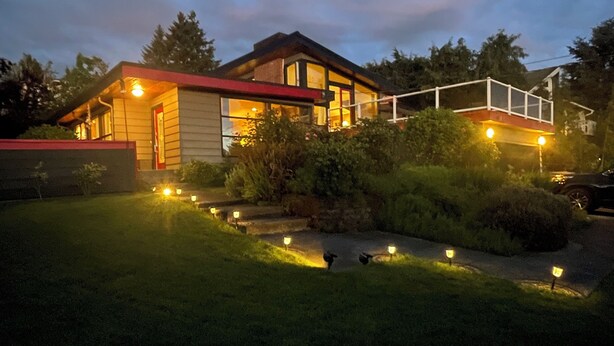 Een modern huis met een goed verlichte voortuin en een overdekt terras.