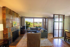 Una sala de estar con chimenea, un conjunto de sofás, un televisor y un amplio ventanal con vistas a zonas verdes.
