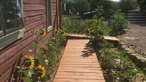 A wooden pathway leading to a red wooden building with large windows and a hanging light fixture. - Historic Pioneer Cabin in the Heart of Canyon Country (Escalante)