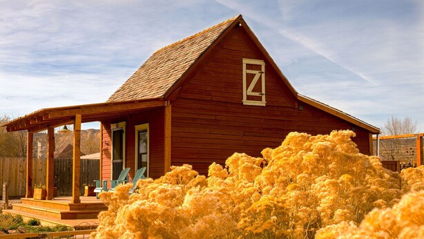 A wooden cabin with a porch, a large window, and a door. - Historic Pioneer Cabin in the Heart of Canyon Country (Escalante)