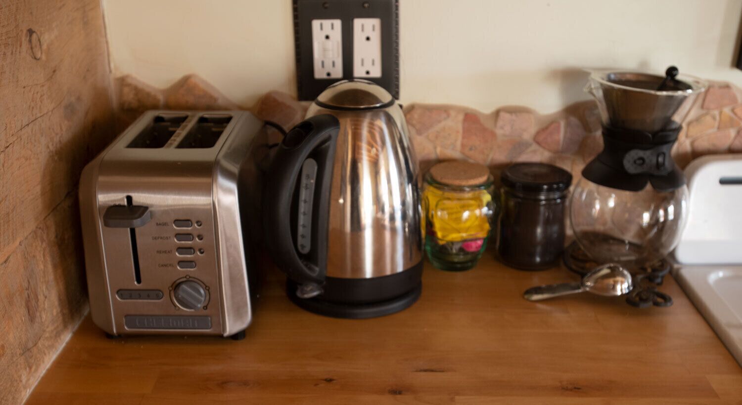 A kitchen counter with a toaster, a kettle, a coffee maker, and some jars.
