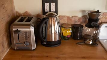 A kitchen counter with a toaster, a kettle, a coffee maker, and some jars.
