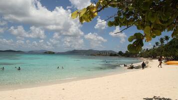 A beach with clear turquoise water, people swimming and walking on the sand, and a clear sky with clouds.
