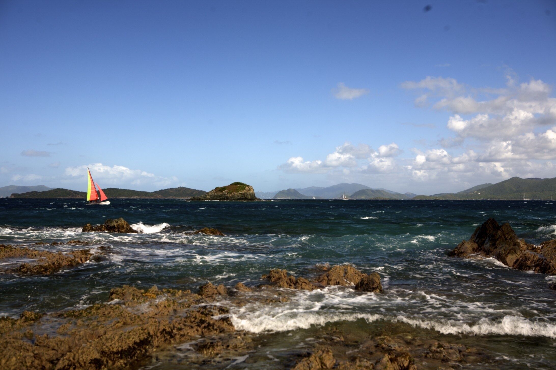 A coastal scene with rocky shores and a sailboat in the distance.