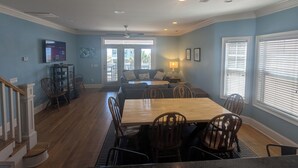 A dining area with a wooden table and chairs, a sofa, and a television on the wall.