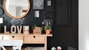 Un comedor con mesa y sillas de madera, un espejo y una pared decorada con cuadros y una pizarra con forma de corazón.