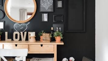 Uma sala de jantar com mesa de madeira, cadeiras, espelho e parede decorada com quadros e um quadro-negro em formato de coração.