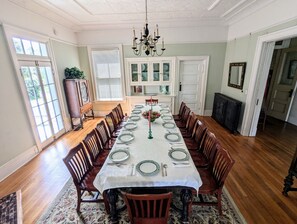 Uma sala de jantar com uma mesa comprida posta para refeição, rodeada por cadeiras de madeira.