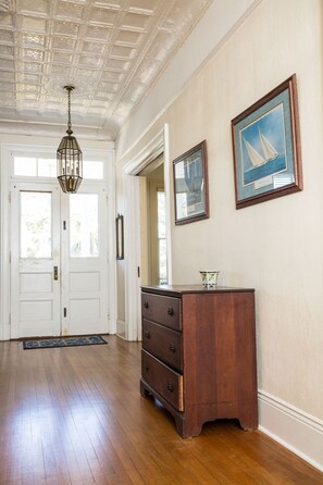 Quarto espaçoso com piso de madeira, um grande aparador de madeira, um candeeiro pendente e duas pinturas emolduradas na parede.