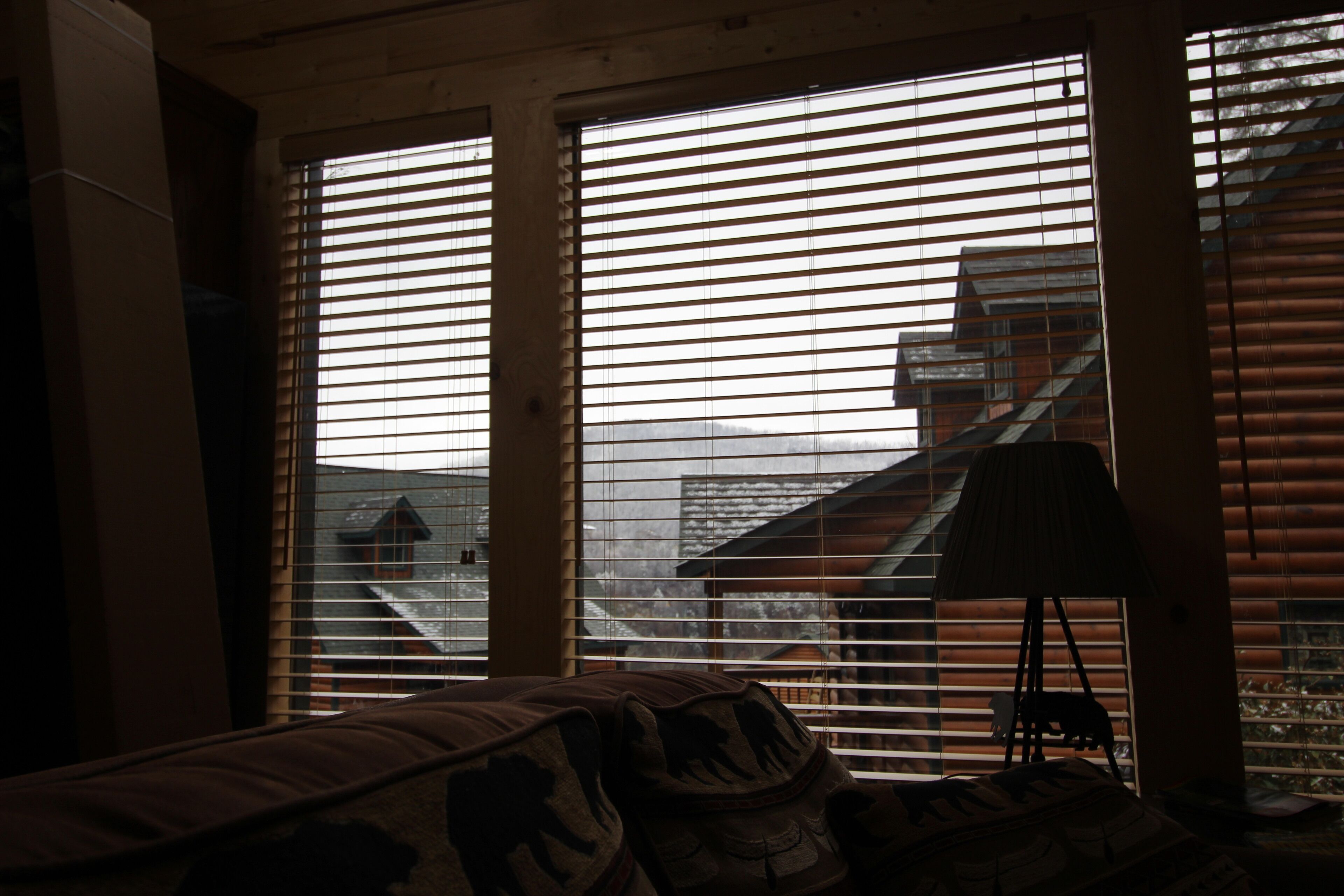 Una habitación con cama, lámpara y vistas a través de amplios ventanales con persianas.