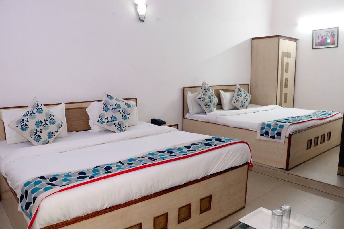 A hotel room with two beds, each with a wooden headboard, white bedding, and blue floral pillows. There is a wardrobe and a small table with a tray of glasses.
