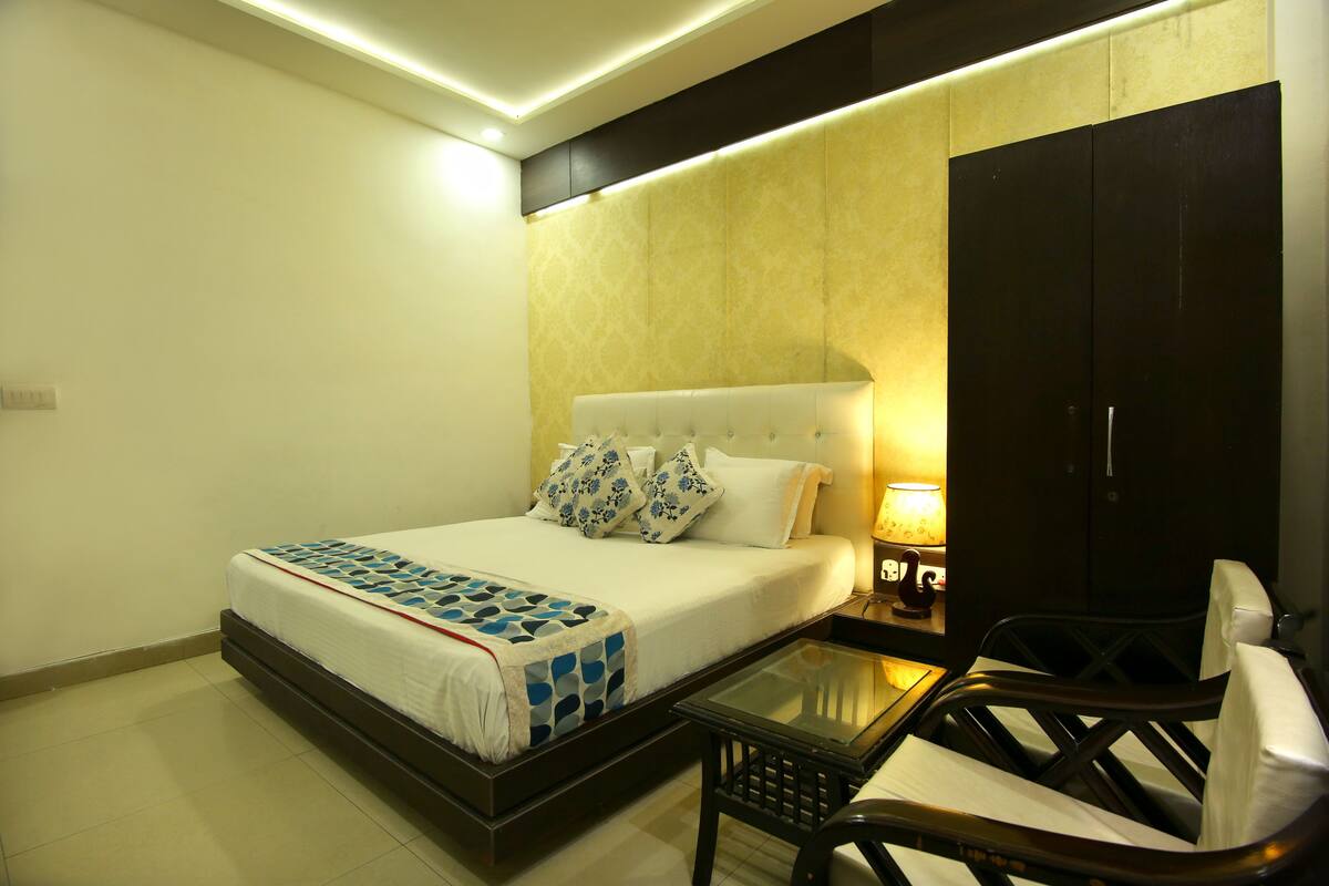 A hotel room with a bed, bedside table, chair, and a nightstand with a lamp.