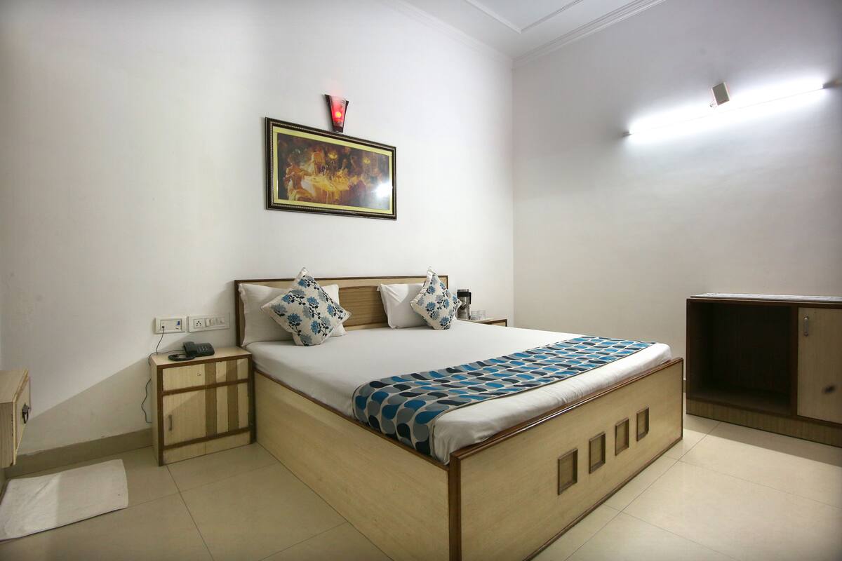 A bedroom with a bed, bedside table, lamp, and a painting on the wall.
