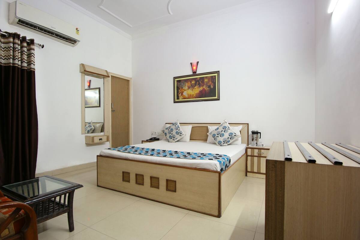 A bedroom with a bed, bedside table, lamp, and a painting on the wall.