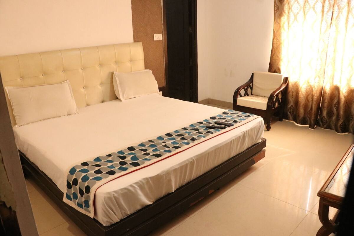 A neatly made bed with a patterned bedspread, a tufted headboard, and a chair with a cushion.