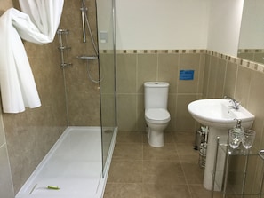 Casa de banho com chuveiro em cabine de vidro, sanita e lavatório com prateleira de vidro.