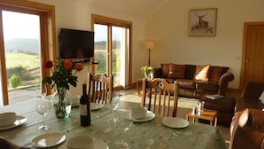 A dining area with a table set for four, a television mounted on the wall, and a sofa in the background. - Torran View (Inverness)