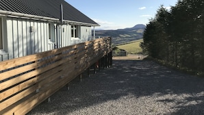 A building with a sloped roof and a gravel driveway leading to a wooden fence. - Torran View (Inverness)